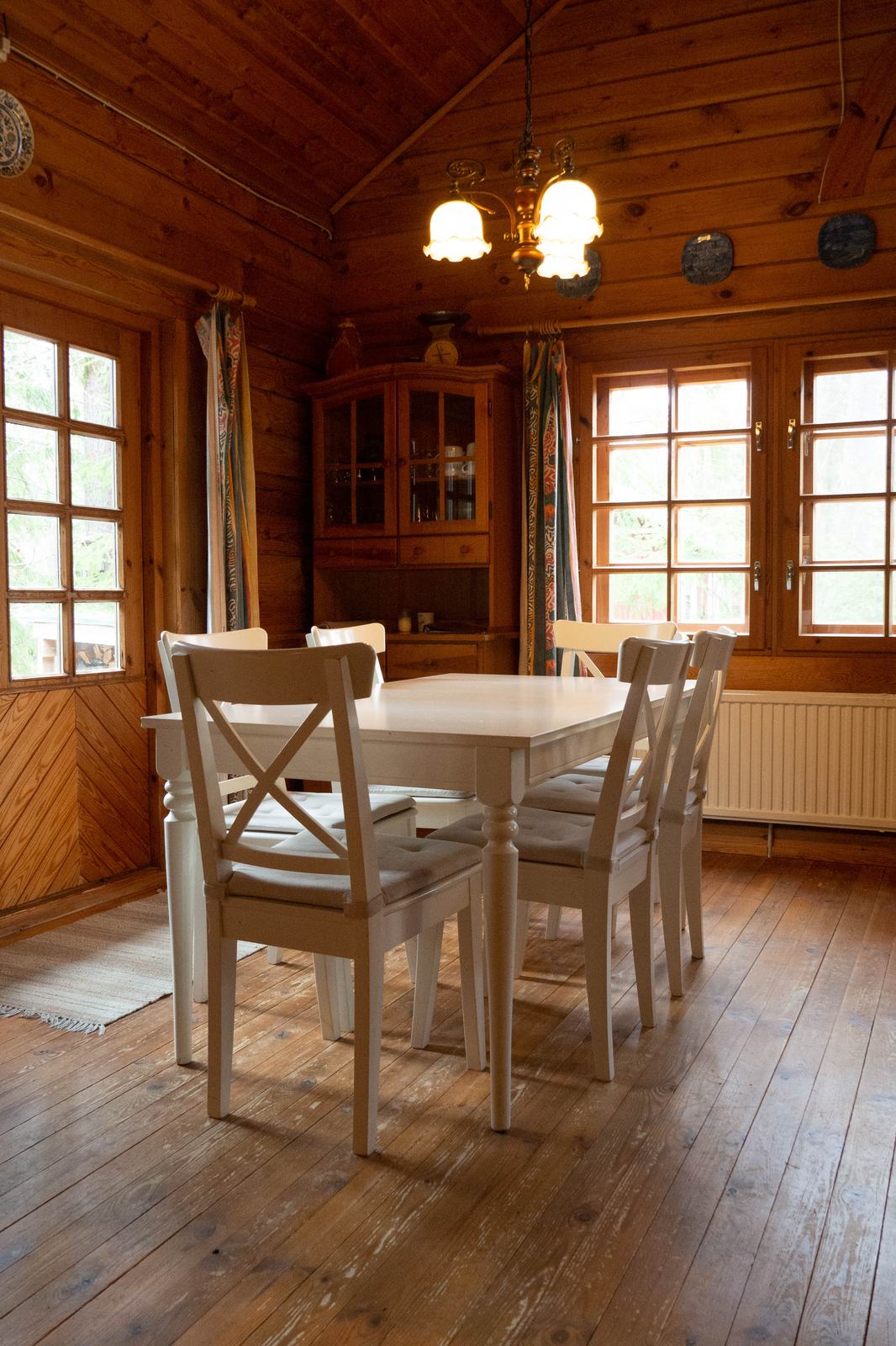 Eethoek met houten tafel en stoelen onder een hoog plafond met kroonluchter